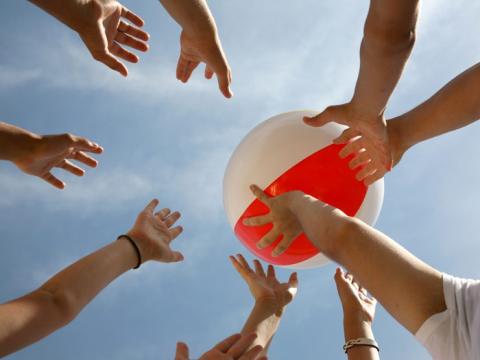 Several children's hands hit a beach ball into the air