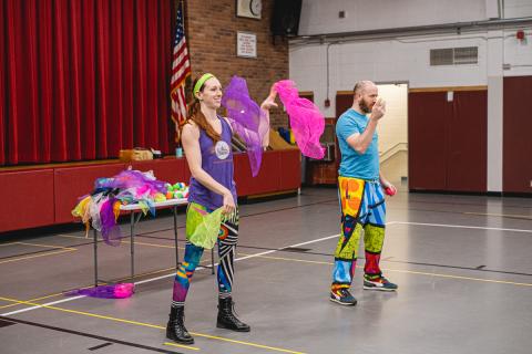 Two colorfully dressed circus performers demonstrate how to juggle