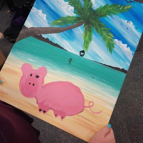 A child has painted a pink pig on a tropical beach