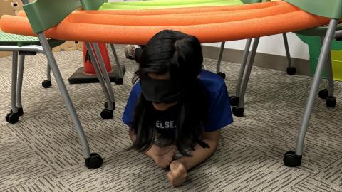 A blindfolded child crawls through an obstacle course.
