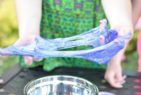 A girl stretches blue slime between her hands.