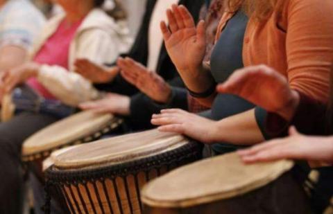 A line of drummers strike their drums with their hands.