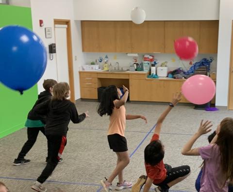 Middle grade children hit balloons into the air