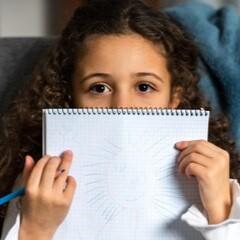 A girl peeks from behind a notebook.