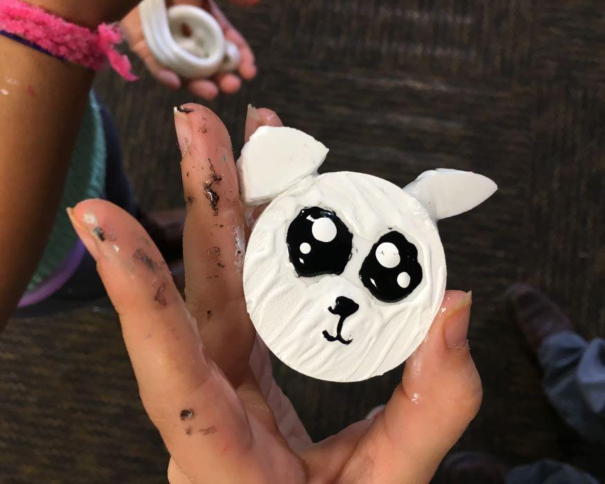 A child's hand holding a a foam circle painted to resemble a panda's face