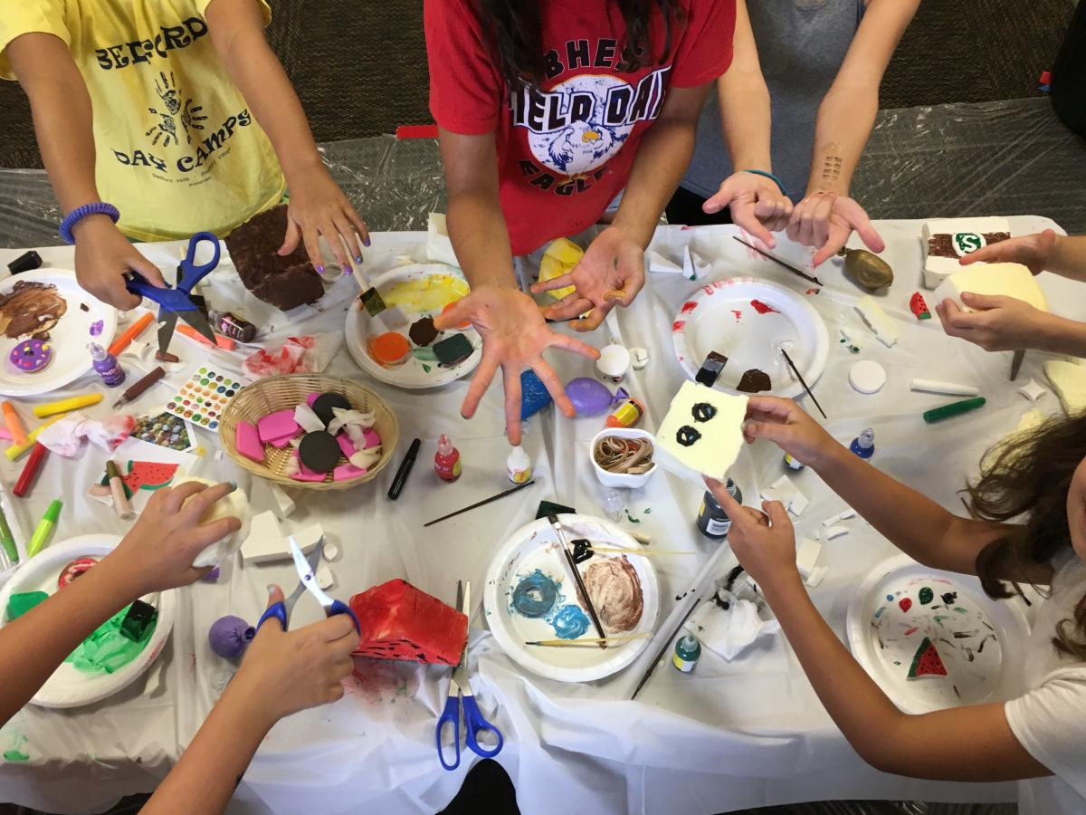 Children craft foam objects on a cluttered tabletop.