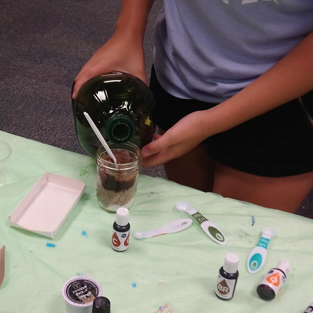 A girl pours a colorful mixture into a cup.
